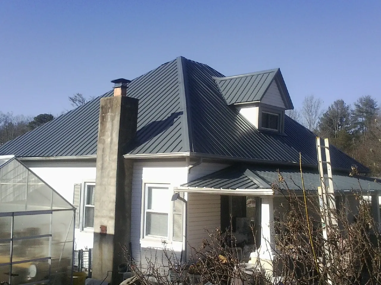 Dark blue standing seam metal roof on a white farmhouse with dormer — Slate & Tile Roof Repair by Roofing Brothers in Richardson
