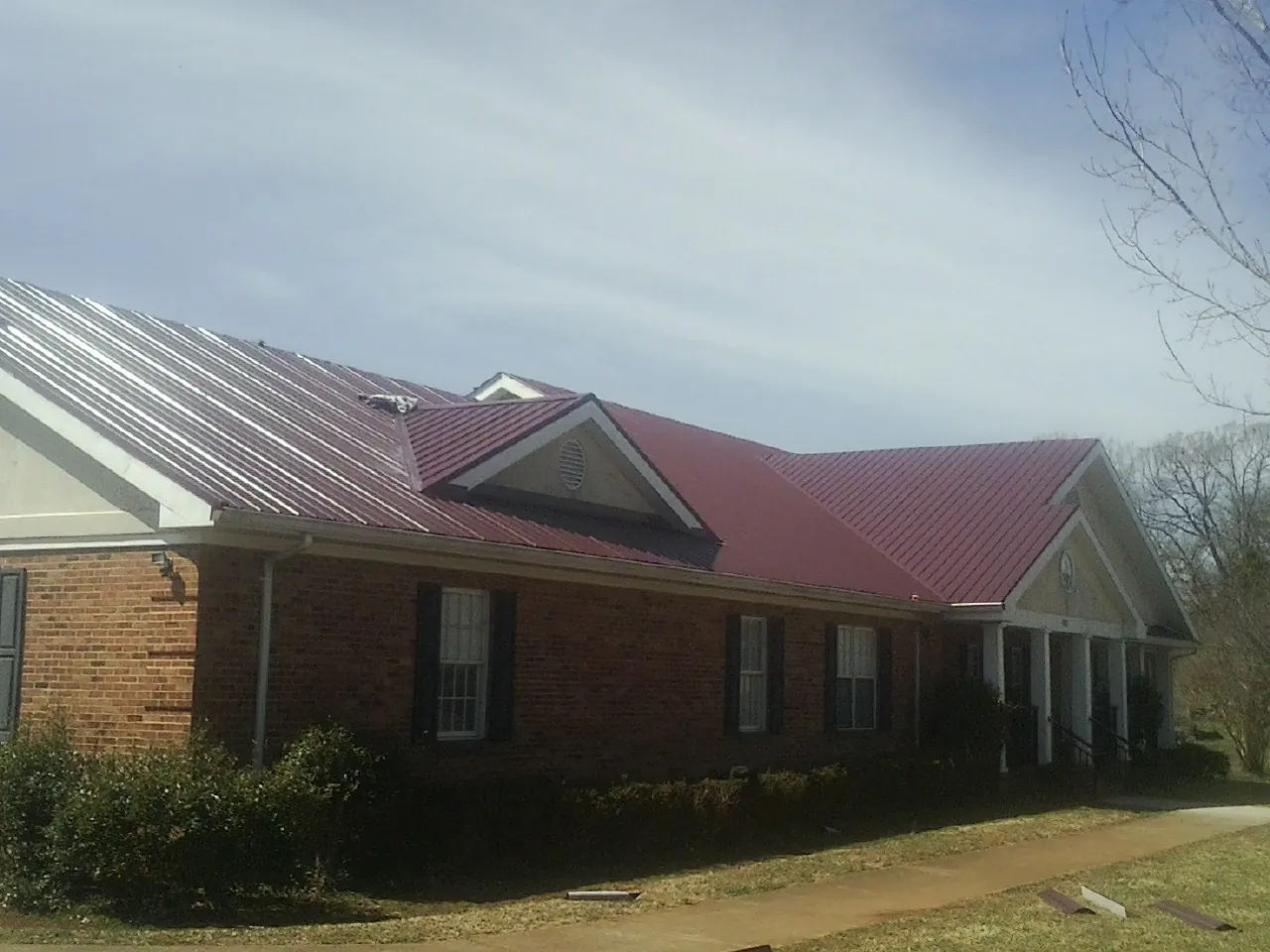 Red metal roof with gabled entries on a long brick building, from a Hail Damage Roof Repair job in Richardson