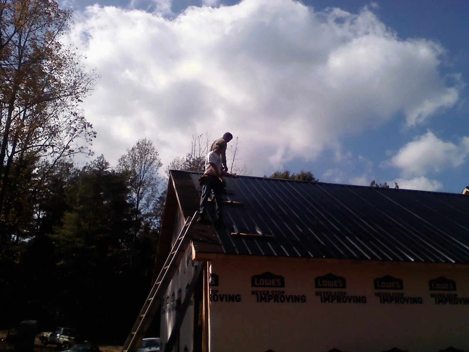 Roofer fastening dark metal panels high against a cloudy sky, from a Roof Inspection job in Richardson